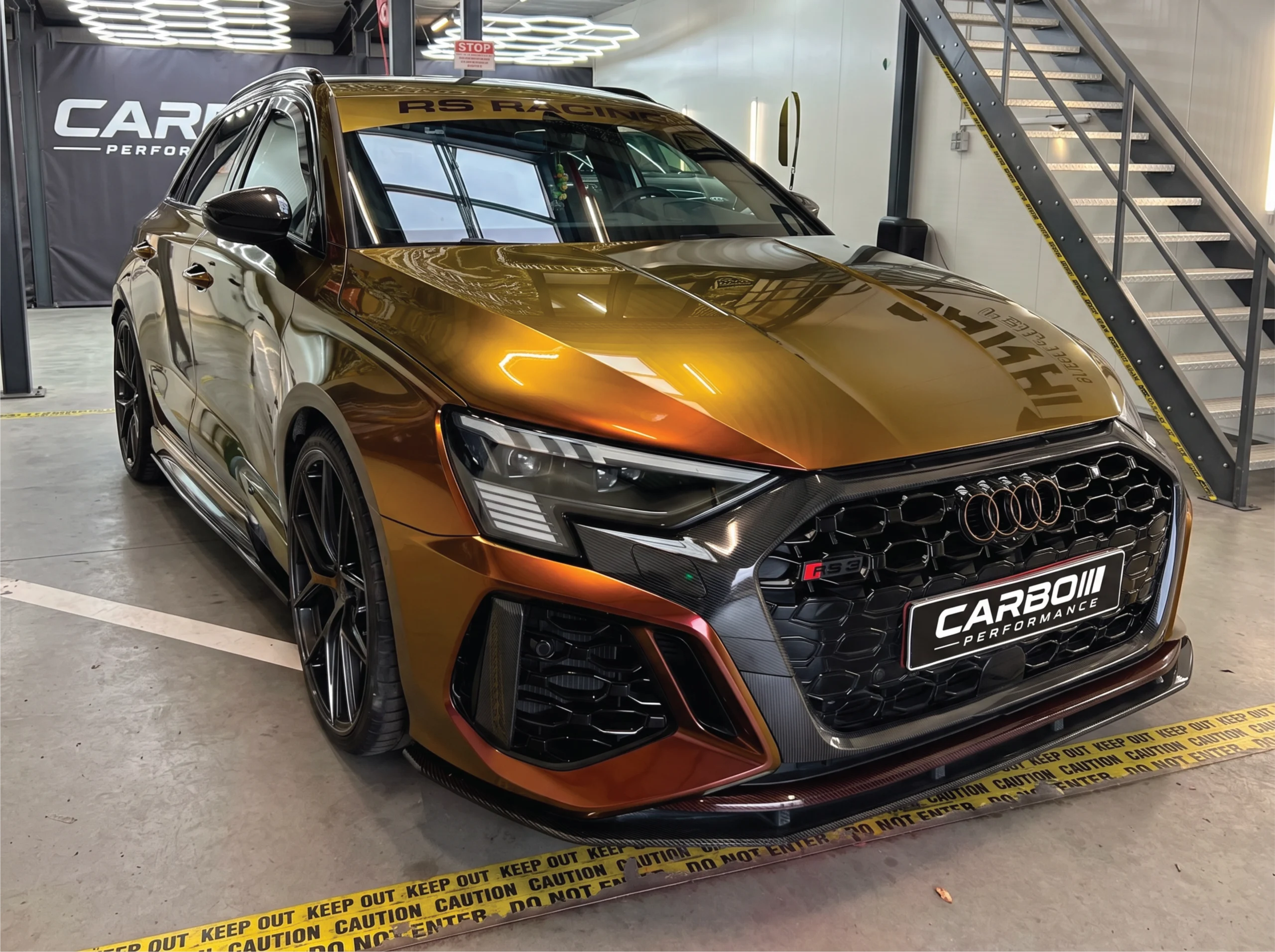 Carbo-Portofilo 14 Audi RS3 Sportback getransformeerd met Ruby Gold car wrap, goudkleurige zonestrip en carbon fiber accenten in de studio