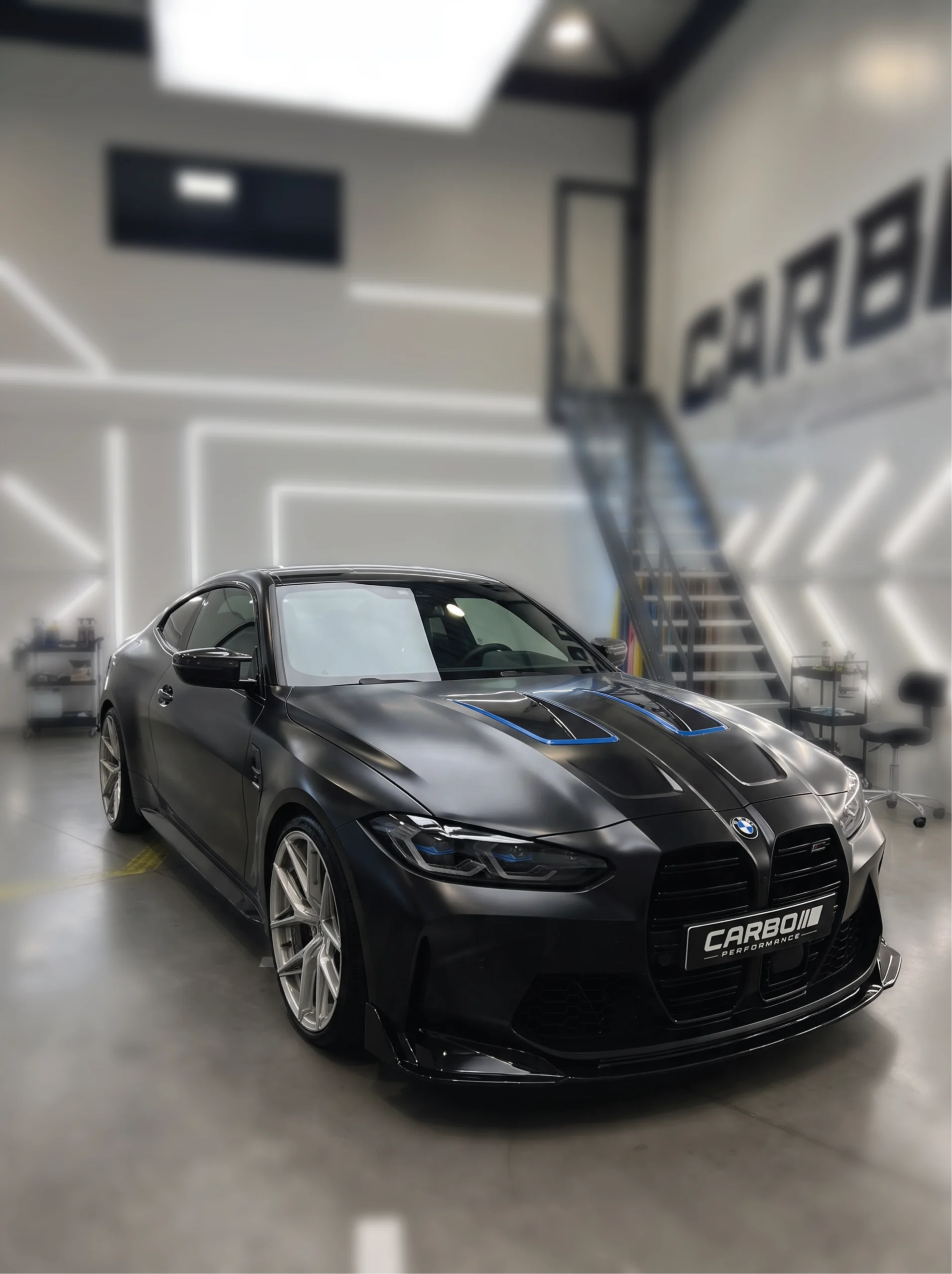 BMW M4 Coupé G82 in Satin Black car wrap met blauwe accenten op de motorkap in de car wrapping studio